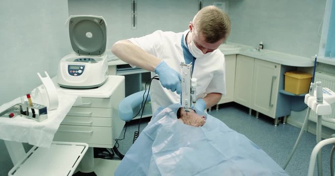 In a cosmetology room doctor make modern procedure for face to his patient , using a modern technology of vampire facial prp , patient laying down on the blue chair.