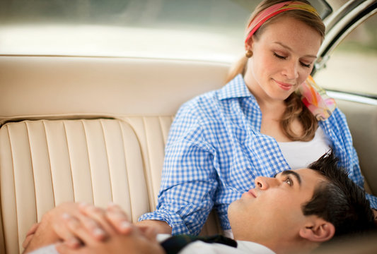 Young adult couple sitting in the back seat of a car.
