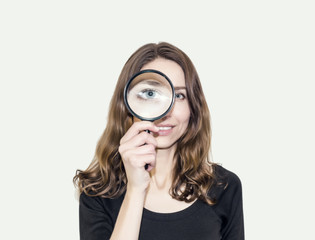 Cute girl with long hair looks at one eye through a magnifying glass