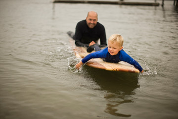 Father and son lying on surfboard.