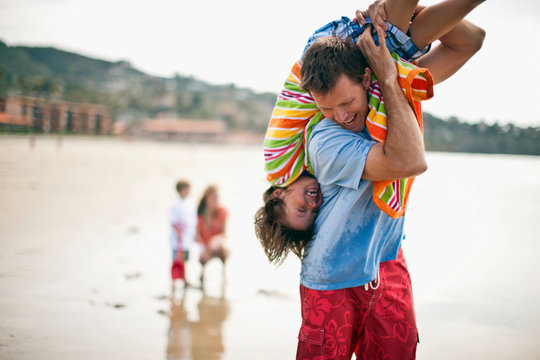 Father carrying his son upside down,  over his shoulder at the beach.