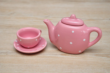 A spotted pink porcelain tea cup and kettle on a wooden background