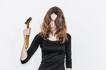 Beautiful girl in a black dress holding a hammer in her hand. Threat, violence, threatens to strike. Hard work, exploitation, release.