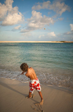 Young boy throwing a stone into the sea on a beach.