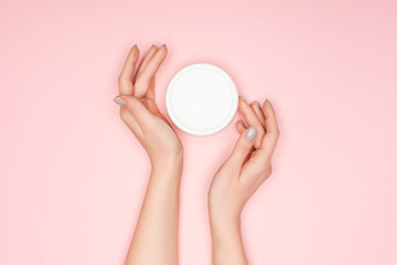top view of female hands with body cream isolated on pink