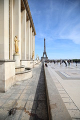 Tourists walk around the building with golden women and the Eiffel Tower is clearly visible