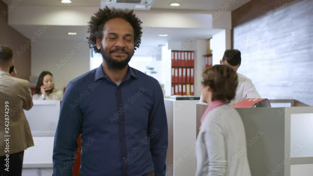 Poster front view of optimistic confident middle eastern man walking through office and saying hello to one