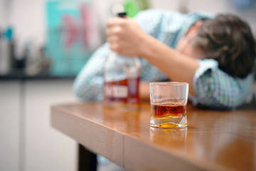 A glass of whiskey on the table on the background of a drunken man. Alcoholic father