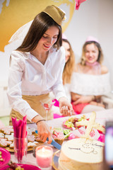 the happy young bride stewardess standing near the festive table at the hen party and cutting a cake