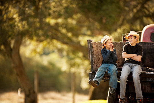 Two young brothers sitting on the back of a pick-up truck in the country and laughing