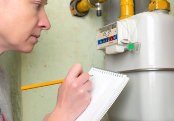 Woman writes indication gas meter in notebook.