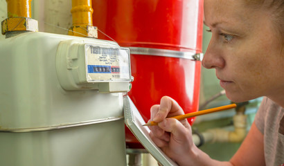 Woman writes indication gas meter in notebook.