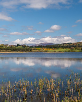 Blue sky and white clouds reflected in a lake water with green hills in the distance. Blessington Lake landscape in Wicklow, Ireland.