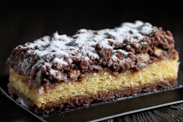 Delicious Kuchen pie with banana, chocolate and powdered sugar on a black background