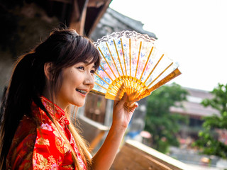 Portrait beautiful asian woman smile wear traditional chinese dress holding a fan looking outside. Festivities and Celebration concept