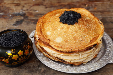 Still life with pancakes and black caviar on a wooden table