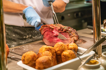 Chef slicing roast beef using carving knife and fork, close up photo
