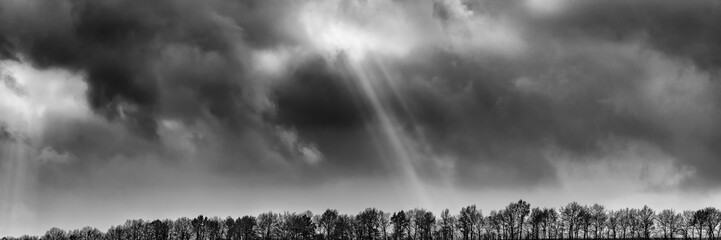 sun rays against the background of clouds and forest in a hilly area, rural landscape. Web banner.