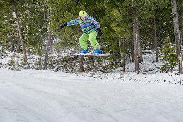 Fototapeta na wymiar Snowboarder jumping in the mountains on a forest background