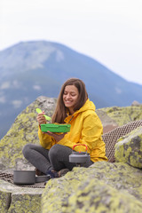 Fototapeta premium Young woman in yellow jacket have a picnic on top of the mountain. 