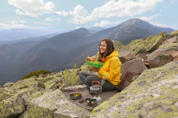 Naklejka premium Young woman in yellow jacket have a picnic on top of the mountain. 