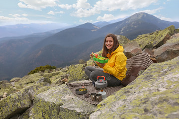 Young woman in yellow jacket have a picnic on top of the mountain. 