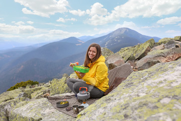 Naklejka na ściany i meble Young woman in yellow jacket have a picnic on top of the mountain. 
