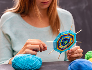 Young girl is doing handmade mandala out of colored yarn.