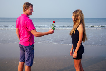Fototapeta premium Valentine's Day February 14th a man gives a woman a rose standing on a beach by the sea summer morning