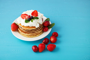 pancakes in a plate with strawberries, mint, honey and cherry on a bright blue background.