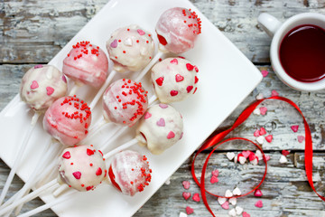 Red velvet cake pops covered in white chocolate decorated with red and pink sugar sprinkles, sweet...