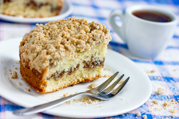 Traditional cinnamon coffee cake piece on a plate and cup of coffee on table