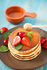 pancakes in a plate with strawberries, mint, honey and cherry on a bright blue background.