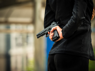 A woman in a business suit holds a gun hidden in the back, a concept of betrayal in business