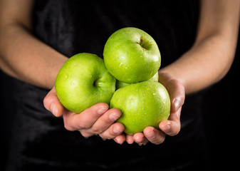 Green apples in woman hands on black background