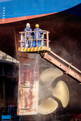 Dock workers work vessel hull ship repair drydock.