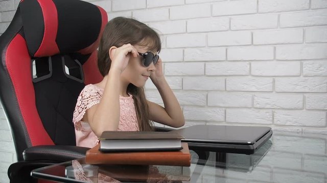Child putting on pinhole glasses. Little girl with obscura glasses at a laptop.