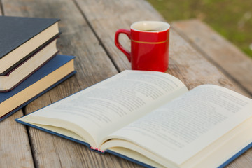 Open book with cup of coffee and pile of closed books on the background.