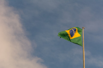 Real Brazilian flag waving against a blue sky.
