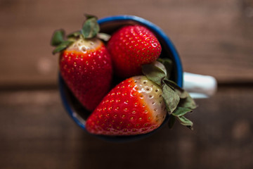several strawberries in a white enamel mug on a wooden table