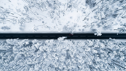 Aerial view of the romantic road passing through the snow-covered winter forest. Top view