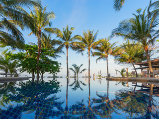 The palm trees from the seashore are reflected in the pool water