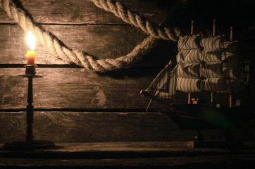 Ship, mooring rope and burning candle on the wooden table. Sea travel concept background. Pirate.