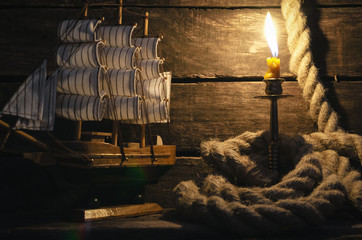 Ship, mooring rope and burning candle on the wooden table. Sea travel concept background. Pirate.