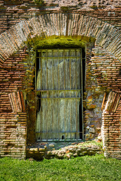 Outdoor front view of one old ancient weathered wooden entrance door and orange brick wall. Roman architecture.