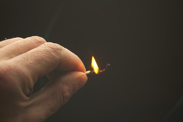 Burning wooden match in hand on dark background