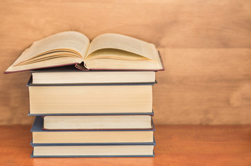 Open book with pile of closed books on wooden background.