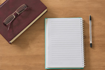 Closed book with blank notebook and glasses on wooden background.