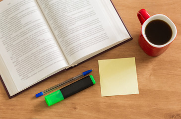 Open book with blank memo pad and cup of coffee on wooden desk background.