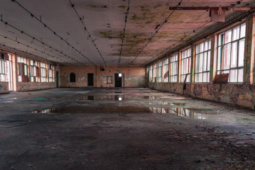 Shabby interior with big windows and reflections in  the puddles on the floor inside the abandoned factory building